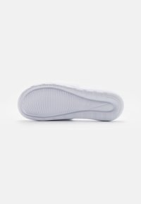 Hvid sneakersål med et tekstureret grip-mønster, der har en glat kurve og et subtilt Nike-logo. Rent, minimalistisk design med afrundede kanter.