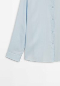 Chemise bleu clair à manches longues avec poignets, boutons visibles sur le devant et tissu uni et lisse.