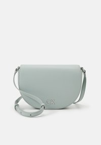 Borsa a tracolla in pelle azzurro chiaro con patta curva e minuteria in argento caratterizzata dal logo "CK". Cinghia regolabile per opzioni di trasporto versatili.