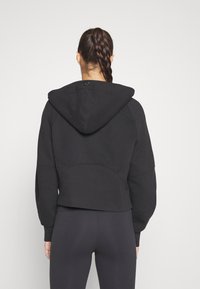 Czarny krótki hoodie z kapturem na sznurki, teksturowana tkanina i sportowe detale w szyciu. Brak widocznych logo lub ozdób.