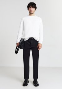 Maglione bianco a trama, pantaloni neri su misura e scarpe stringate. Porta una borsa nera con due manici. Design minimalista, colori neutri.