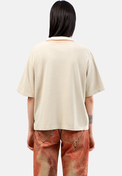 Beige oversized t-shirt med korte ærmer, blød tekstur og detaljer med udskæring på ryggen, parret med røde mønstrede bukser med elementer af denim-design.