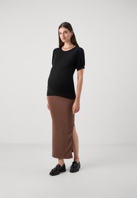 Svart ribbad topp med korta puffärmar, kombinerad med en brun ribbad midikjol med en sidoklyfta. Modellen bär svarta loafers.
