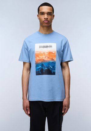 Lyseblå bomulds T-shirt med et frontgrafik af orange og blå bjerglandskab med teksten "Napapijri geographic" ovenfor. Korte ærmer.