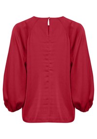 Czerwona bluzka z okrągłym dekoltem i zapięciem na guziki z tyłu. Posiada bufiaste rękawy zebrane w mankietach oraz gładką teksturę.