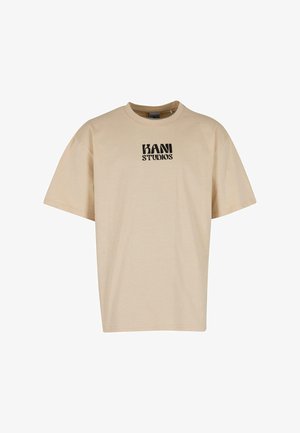 Beige katoenen t-shirt met korte mouwen, ronde hals, met een zwart "KANI STUDIOS" logo aan de voorkant. Zachte textuur, ontspannen pasvorm.
