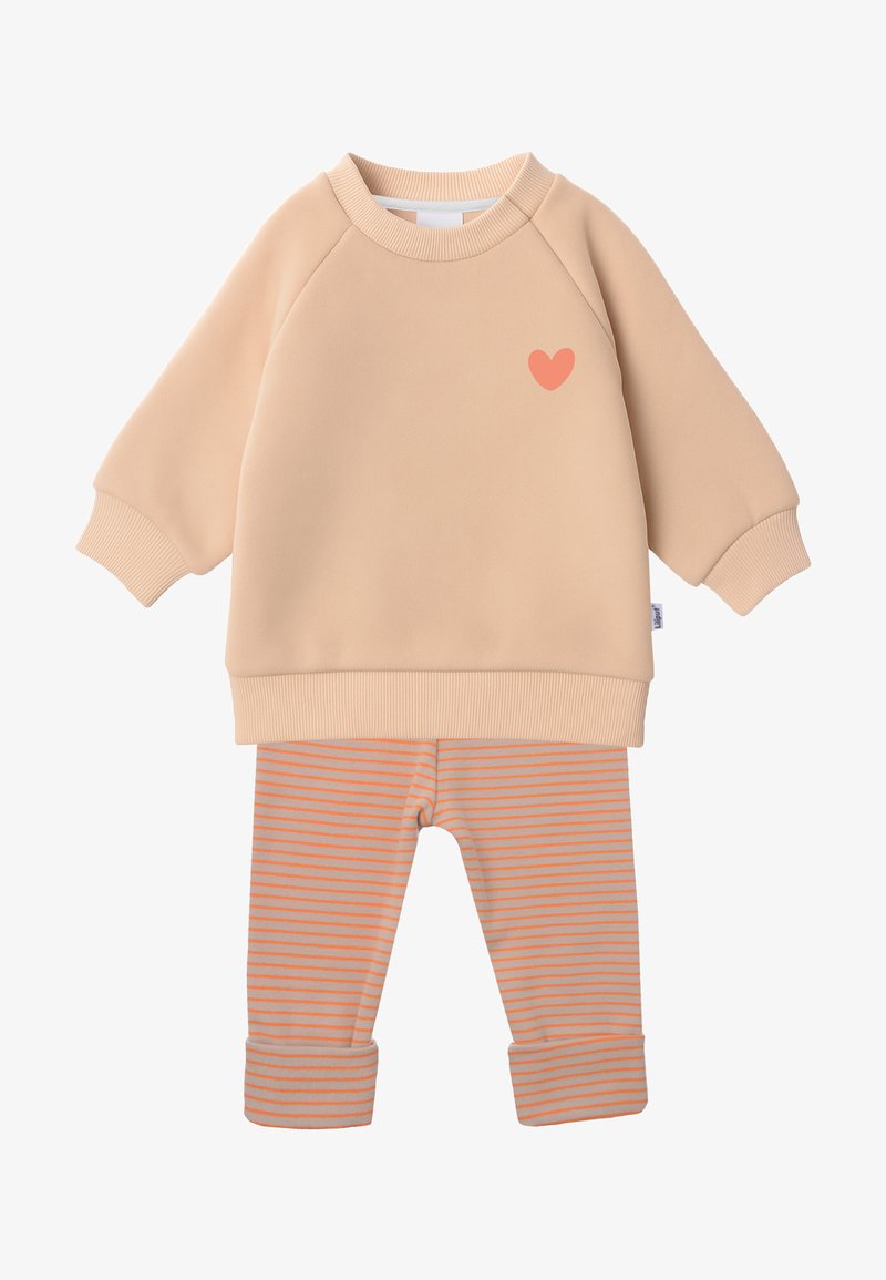 Pfirsichfarbenes Sweatshirt mit einem kleinen orangen Herz-Graphic, kombiniert mit gestreiften, hellgrauen und orangenen Leggings mit umgenähten Säumen.