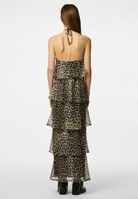 Robe maxi sans manches imprimée léopard avec un design en volants superposés, tissu léger, lien à nouer autour du cou, et une silhouette fluide.
