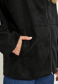 Svart zip-up jacka i mjukt tyg, med sidfickor, långa ärmar och en slät yta med en ren design.