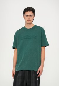 Tmavozelené bavlnené tričko s vypuklým logom "adidas" na hrudi. Krátke rukávy a výstrih typu crew neck.