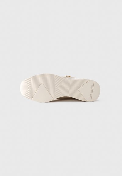 Semelle de sneaker beige avec des motifs de grip texturés et le logo "MICHAEL KORS" près du talon.