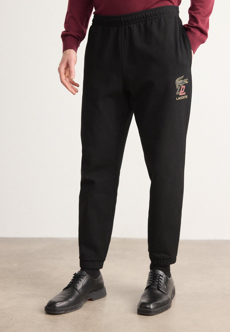 Zwarte sweatpants met een elastische tailleband, vergrendelde enkels en een opvallend geborduurd logo met gouden accenten op de dij.