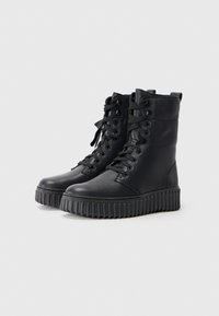 Bottines en cuir noir avec un haut texturé, un laçage à l'avant et une semelle en caoutchouc épaisse dotée d'un design rainuré.