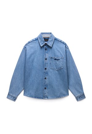 Camisa de manga larga de mezclilla azul claro, con botones, cuello y bolsillo frontal que presenta un pequeño detalle bordado oscuro.