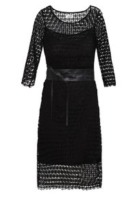 Robe en dentelle noire avec manches trois-quarts, texture semi-transparente, encolure ronde et ceinture en cuir noir à la taille.