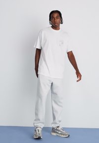 White cotton t-shirt with a chest pocket and graphic print. Light gray sweatpants with ribbed cuffs. Athletic sneakers with a multi-colored design.