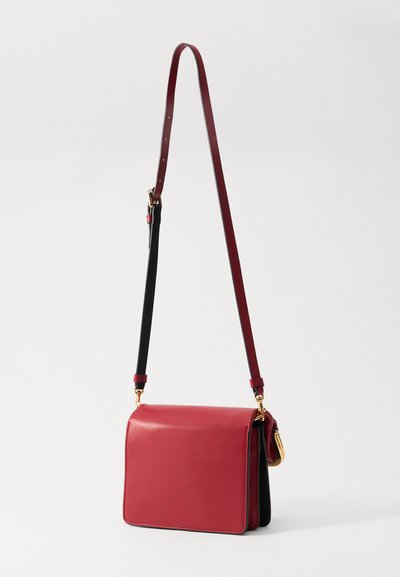 Rød læder crossbody taske med en struktureret form, sorte accenter, en slank justerbar skulderrem og gyldne hardware detaljer.