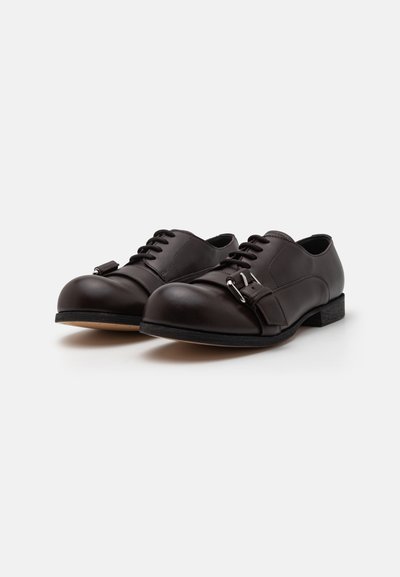 Brown leather shoes with a smooth finish, lace-up design, rounded toe, and a distinctive buckle detail on the side. Rubber sole.