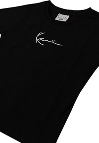 Must t-särk, lühikesed varrukad, must, valmistatud puuvillast, esiküljel valge tikkimismärgiga. Klassikaline ümmargune kaelus. Sile tekstuur.