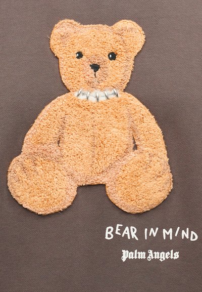 Καφέ ύφασμα με κεντημένη υφασμάτινη αρκουδίτσα σε πορτοκαλί με μαύρα μάτια, φοράει λευκό γιακά. Το κείμενο γράφει "BEAR IN MIND" και "Palm Angels".