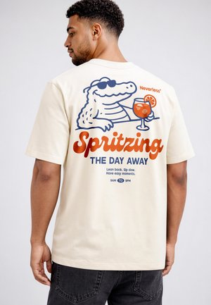 Man wearing cream shirt with cartoon alligator in sunglasses holding a drink, text reads "Spritzing the day away."