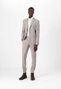 Fato cinza claro, ajustado, com um padrão de xadrez subtil, combinado com uma camisa branca e botins de camurça castanhos. Design slim fit.