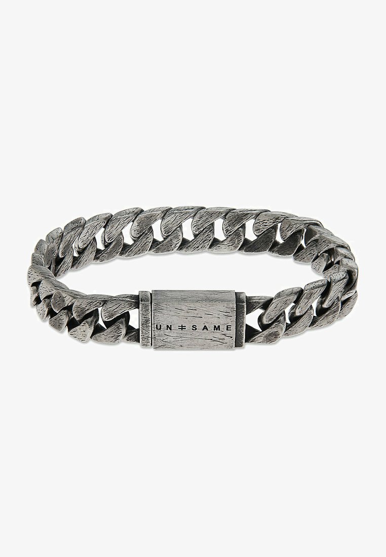 Silverfärgad metallarmband med ett vävt kedjemönster, en texturerad yta och ett rektangulärt spänne med "UN=SAME" ingraverat.