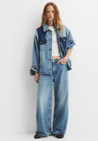 Denimska jakna z lahkim in temnim pranjem, oversize kroj, z dvema žepoma na prsih, v kombinaciji s širokimi svetloblue džinsami. Teksturiran denim finiš.