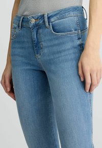 Světle modré džínové kalhoty mají slim fit, středně vysoký pas, přední kapsy a jemné švy podél švů.