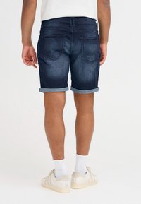 Sötétkék farmer rövidnadrág felhajtott szegéllyel és két hátsó zsebbel. Fehér zoknival és világos színű tornacipővel viselve.