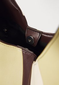 Κοντινή λήψη της εσωτερικής πλευράς μιας μπεζ και σκούρας καφέ δερμάτινης τσάντας με μαγνητική κλείσιμο και μαύρη υφασμάτινη επέν�δυση.