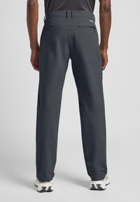 Herren-Hose in Dunkelgrau aus glattem, leichtem Stoff, mit einer Reißverschluss-Rückentasche und einem verstellbaren Bund. Kombiniert mit Sneakers.