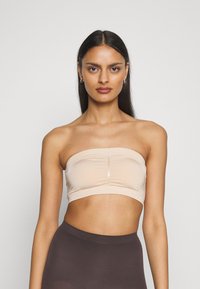 Nude strapless bralette i slätt tyg, med en central söm och elastisk nederkantsband, parat med högmidjade mörka shorts.