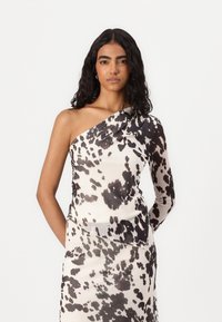 Haut asymétrique avec un imprimé zèbre noir et blanc, conçu en tissu transparent, avec une seule manche longue, texture lisse.