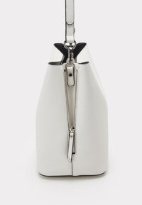 Witte lederen emmer tas met een gestructureerde afwerking, voorzien van een bovenzipper, zilveren hardware en een contrasterende zwarte binnenkant.