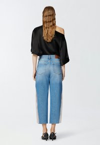 Crna satenska majica s širokim rukavima; traperice visokog struka u plavoj boji s ravnim nogavicama i posvijetljenim bočnim panelima. Crne štikle.