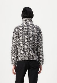Pull en polaire avec col montant, présentant un motif floral noir et blanc. Texture douce, coupe décontractée et ourlet côtelé.