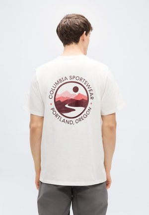 Bombažna majica kremne barve z okroglim motivom na hrbtu, ki prikazuje gore, reko in napis "Columbia Sportswear, Portland, Oregon."