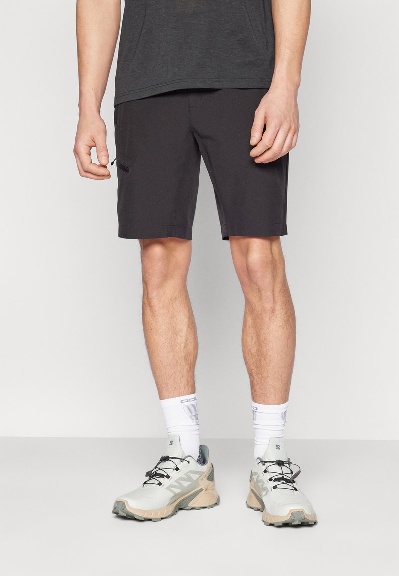 Svarta shorts i lätt material, med en sidoficka med dragkedja och rak passform, kombinerat med grå och beige sportskor.