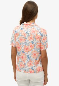 Koszula z krótkim rękawem z lekkiego materiału, zdobiona żywym kwiatowym wzorem w odcieniach różu i niebieskiego na białym tle, o luźnym kroju.