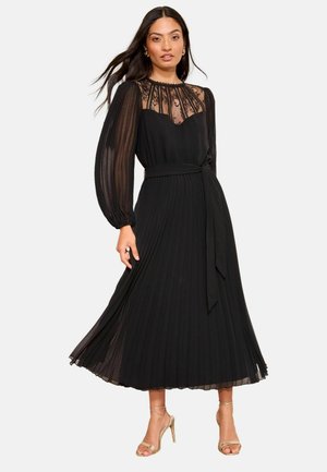 Schwarzes, plissiertes Kleid mit einer transparenten Spitzenblende und langen, gepufften Ärmeln. Enthält einen passenden Stoffgürtel und reicht bis zur Mitte der Waden.