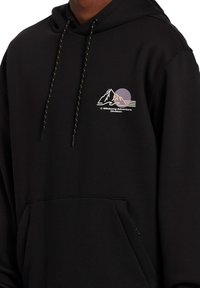 Schwarzer Kapuzenpullover mit einem Logo, das Berge und ein kreisförmiges Design zeigt. Enthält eine Fronttasche und einen Kordelzug mit gemusterten Akzenten.