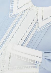 Hellblauer plissierter Stoff mit weißen dekorativen Rändern, die geometrische Ausschnittmuster zeigen.