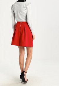 Maglione grigio a maniche lunghe, gonna rossa plissettata con zip posteriore e scarpe nere con tacco alto. La gonna ha un tessuto testurizzato.