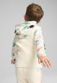 Sudadera crema con siluetas humanas abstractas y coloridas en verde, rosa y azul marino, contrastadas por mangas sólidas crema y pantalones a juego.