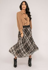 Blouse marron avec des détails en volants, associée à une jupe à motifs noir et crème. Des bottines noires à la cheville complètent la tenue. Texture satinée sur l'ensemble.