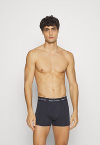 Tummanharmaat bokserit, jotka on valmistettu pehmeästä kankaasta ja joissa on musta vyötärönauha valkoisella logotekstillä. Muotoilu on vartalonmyötäinen ja saumaton.