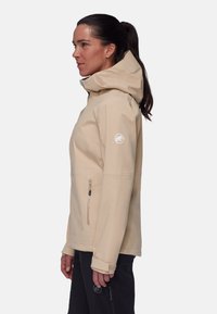 Helle beige wasserdichte Jacke mit Kapuze, seitlichem Reißverschlussfach und elastischen Bündchen. Verfügt über ein Logo auf dem oberen Arm und eine glatte Textur.