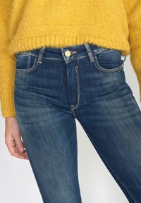 Skinny jeans made of dark blue denim with a classic five-pocket design, featuring a zip fly and gold button detail.