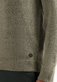 Gebreide trui in gedempt olijfgroen, met een gestructureerde stof, ribgebreide manchetten en onderzoom, en een zwart label aan de onderzijde.